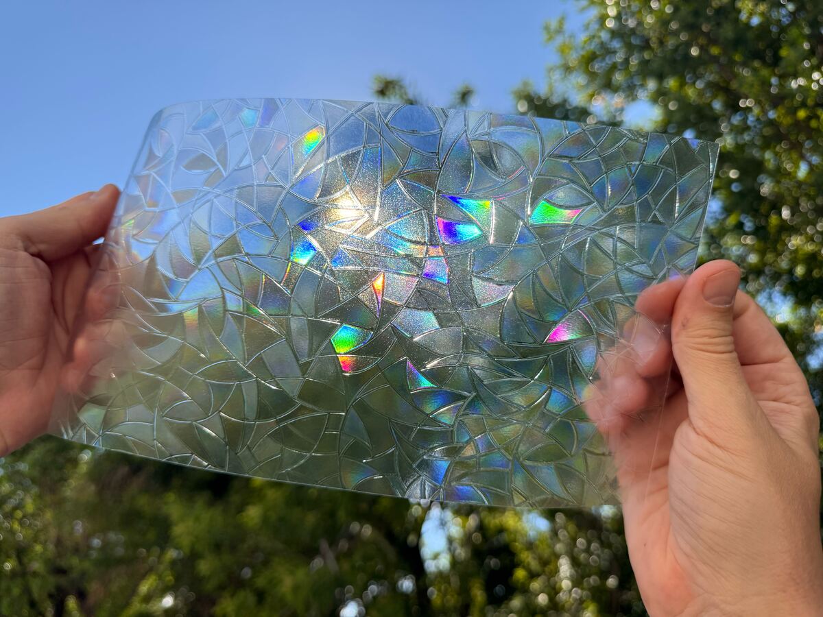 A sheet of SHINECOR rainbow film held up to the sun: small rainbow flecks glow in its mosaic pattern.